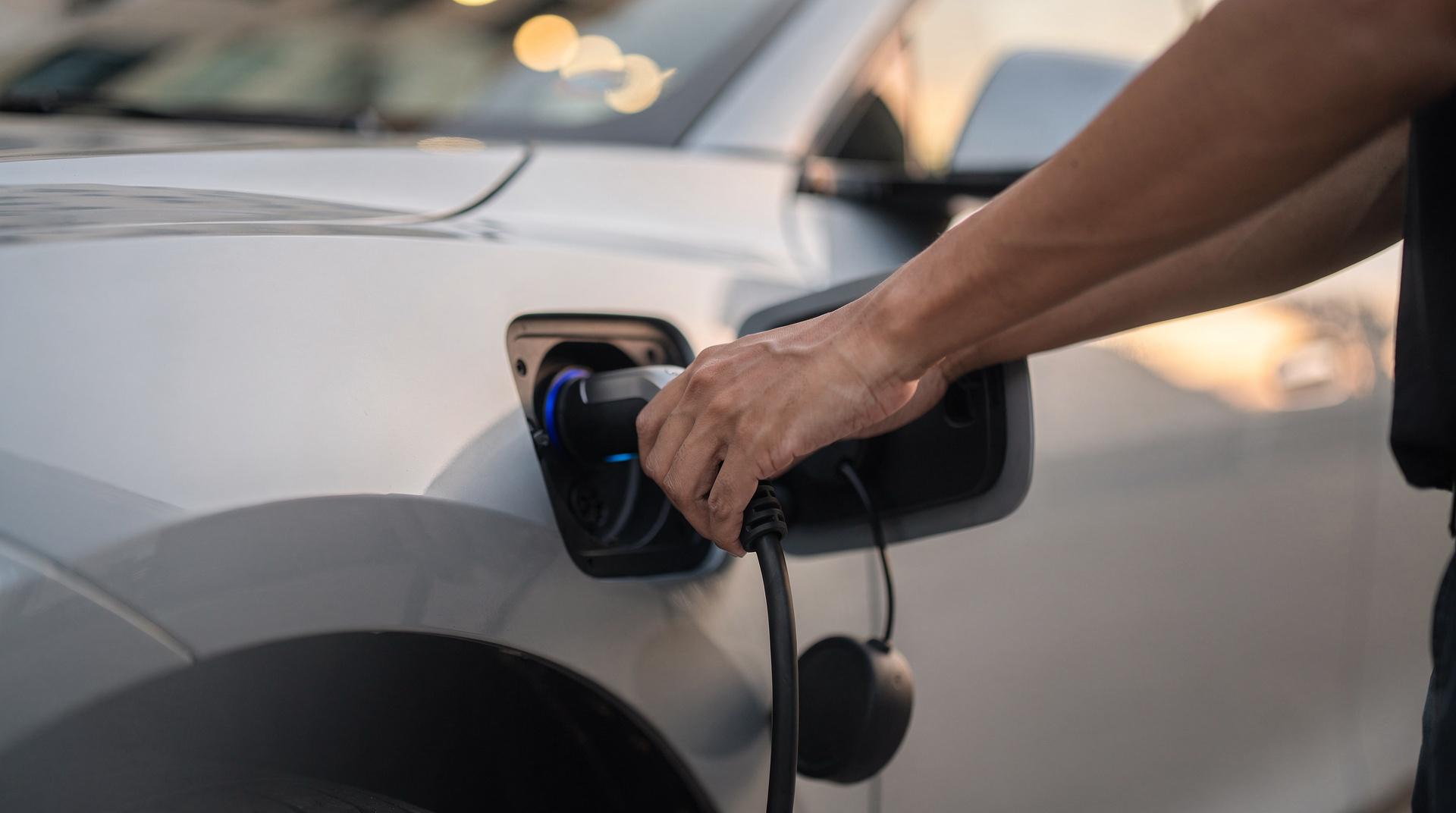 Mains qui branchent un câble de recharge sur une voiture électrique